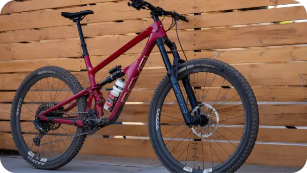 A red Revel Rail mountain bike with a water bottle, parked against a wooden fence.